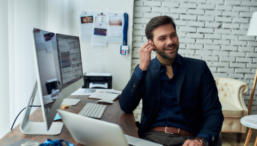 Good talk. Young successful businessman or sales manager wearing wireless earphones, talking with client or partner and smiling, working in the modern office